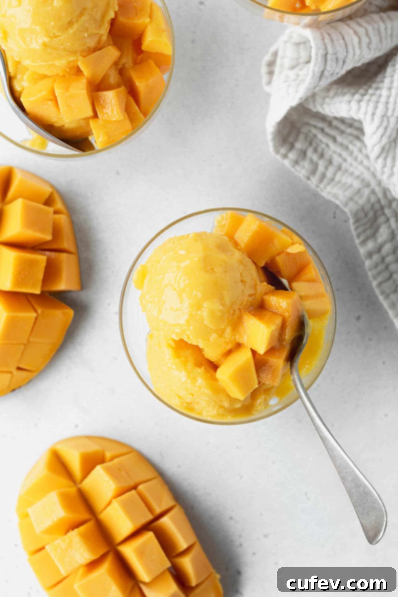 Two Ingredient Mango Sorbet 7 Mango sorbet scoops in a bowl, garnished with fresh mango chunks and a sprig of mint