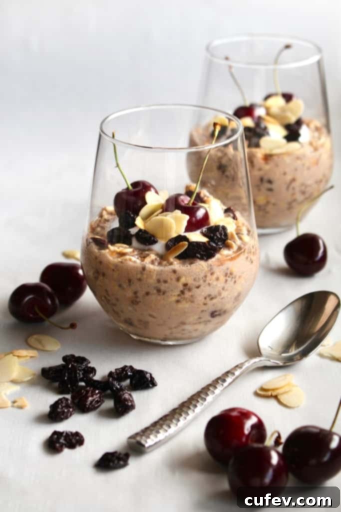 Glass tumblers with overnight oats inside with fresh cherries, dried cherries, and sliced almonds scattered around.