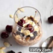 Overnight oats in a glass topped with yogurt, dried cherries, sliced almonds, and two fresh cherries on top.