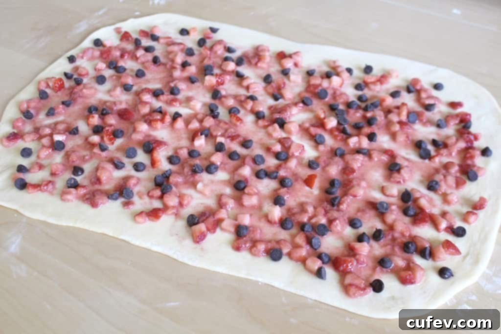 Rolled out dough rectangle spread with vibrant strawberry filling and sprinkled with chocolate chips.