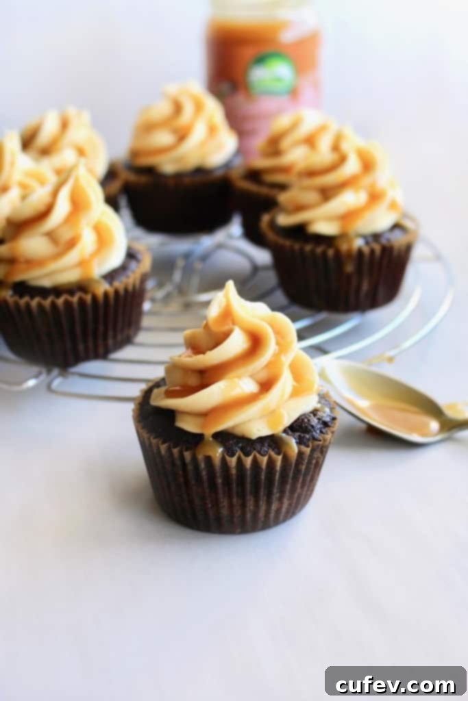A beautifully frosted vegan salted caramel chocolate cupcake, demonstrating the smooth texture and elegant piping of the salted caramel buttercream, with a drizzle of extra caramel.