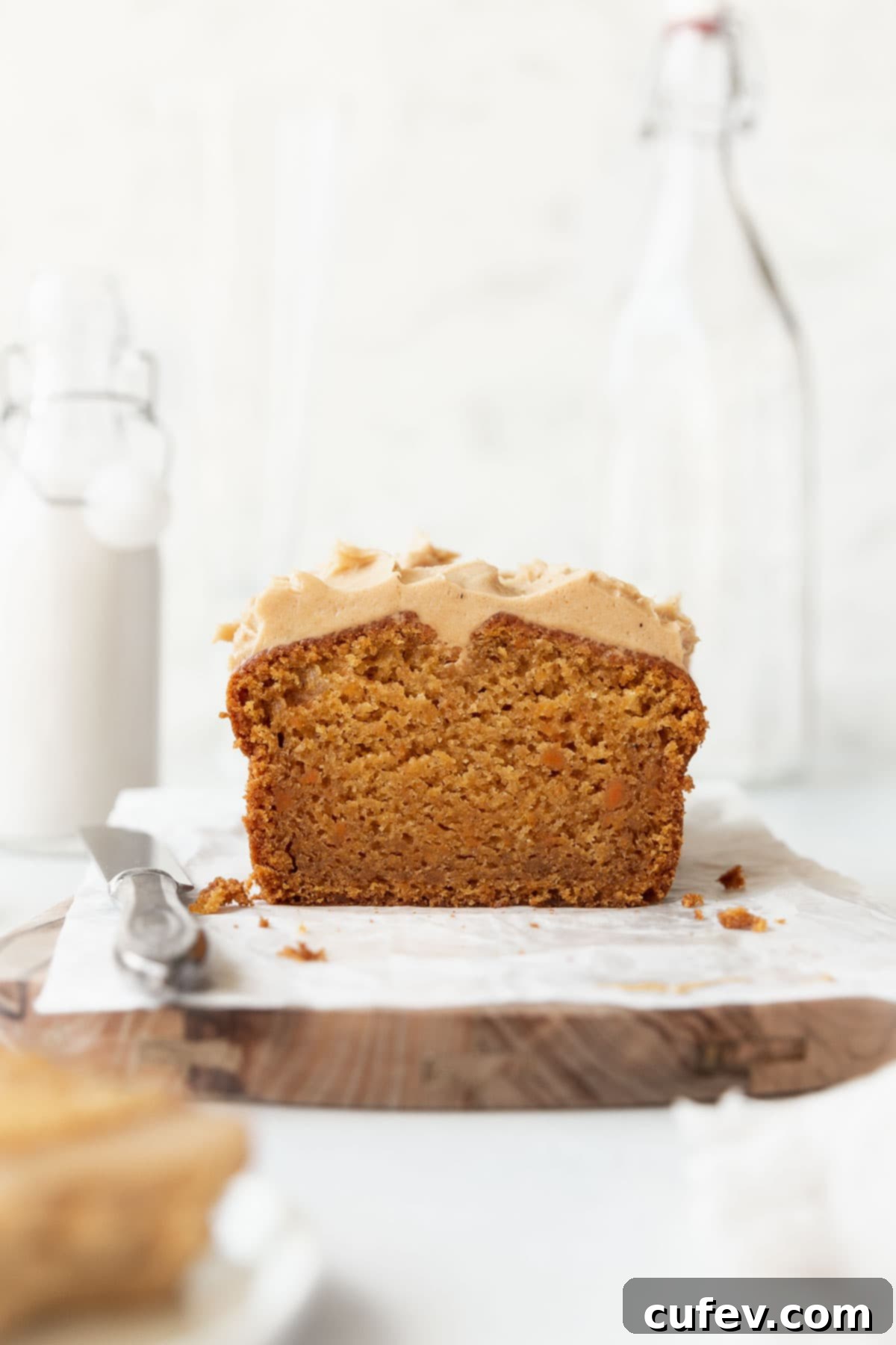 Straight on shot of a beautifully frosted sweet potato cake with creamy maple cashew frosting, presented on parchment paper over a rustic wooden board. Perfect for fall.