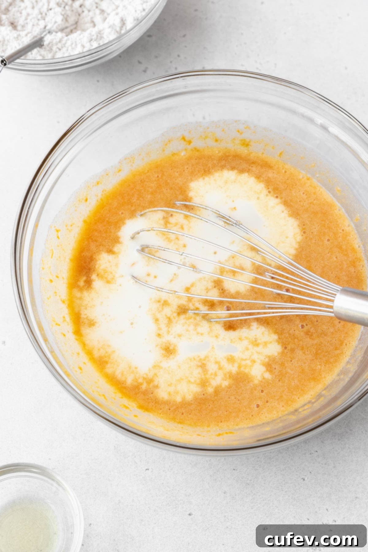 Non-dairy milk has just been whisked into the glass bowl containing the other wet ingredients, creating a smooth and cohesive mixture.