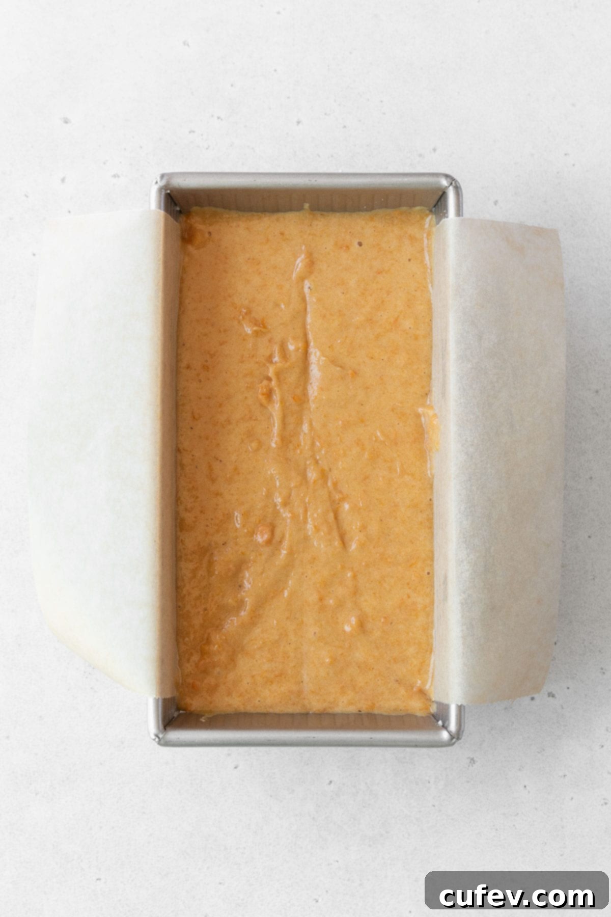 A freshly baked gluten-free sweet potato loaf cooling in a metal loaf pan, lined with parchment paper for easy removal.