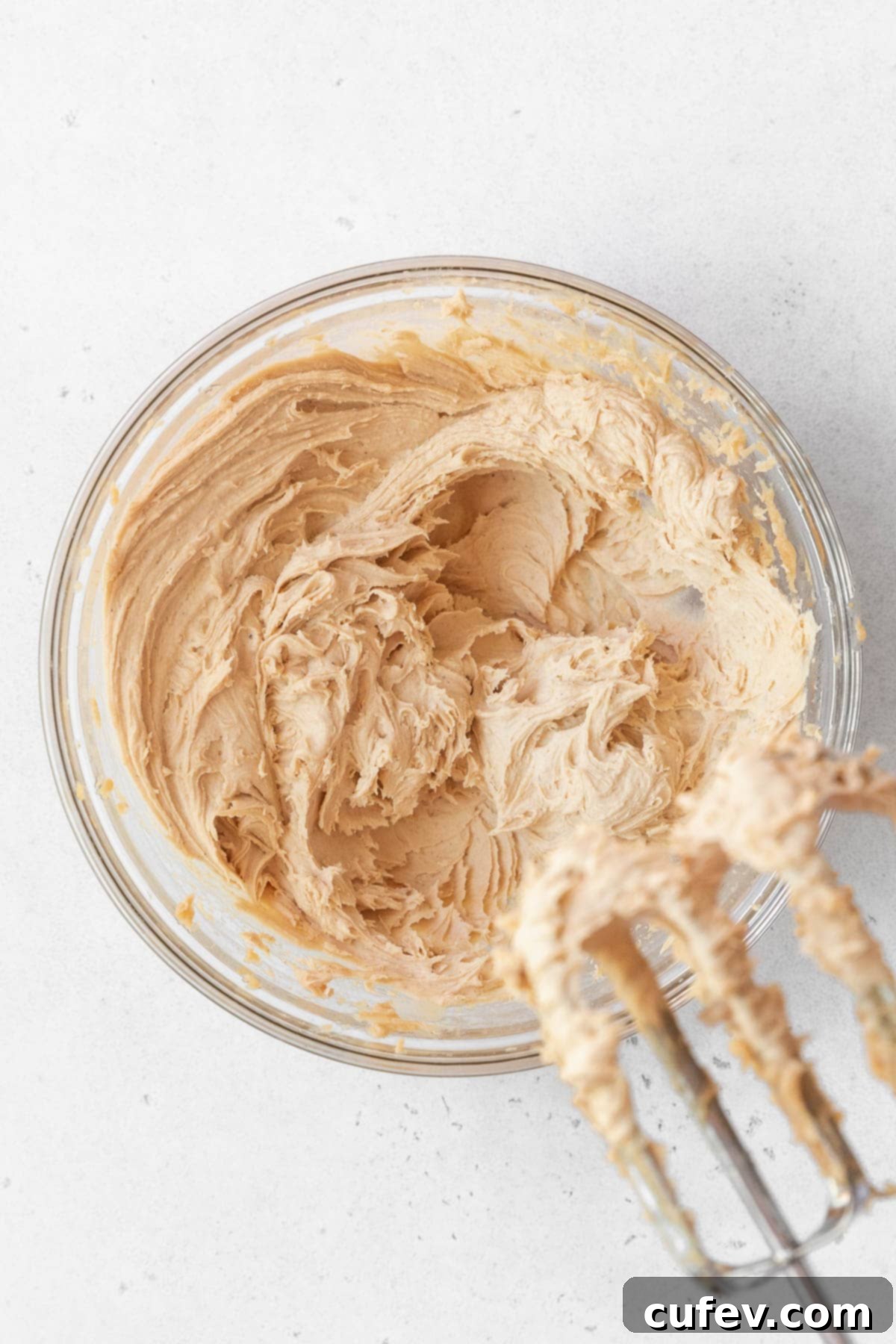 A glass bowl containing the cashew frosting, now light and airy, being whipped with a hand mixer to achieve its perfect consistency.
