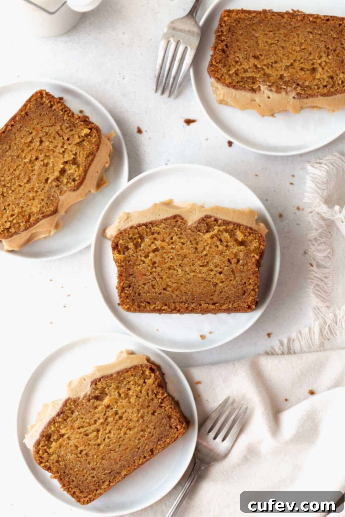Overhead shot of perfectly cut sweet potato cake slices arranged on elegant white dessert plates, accompanied by silver forks on a clean white surface.