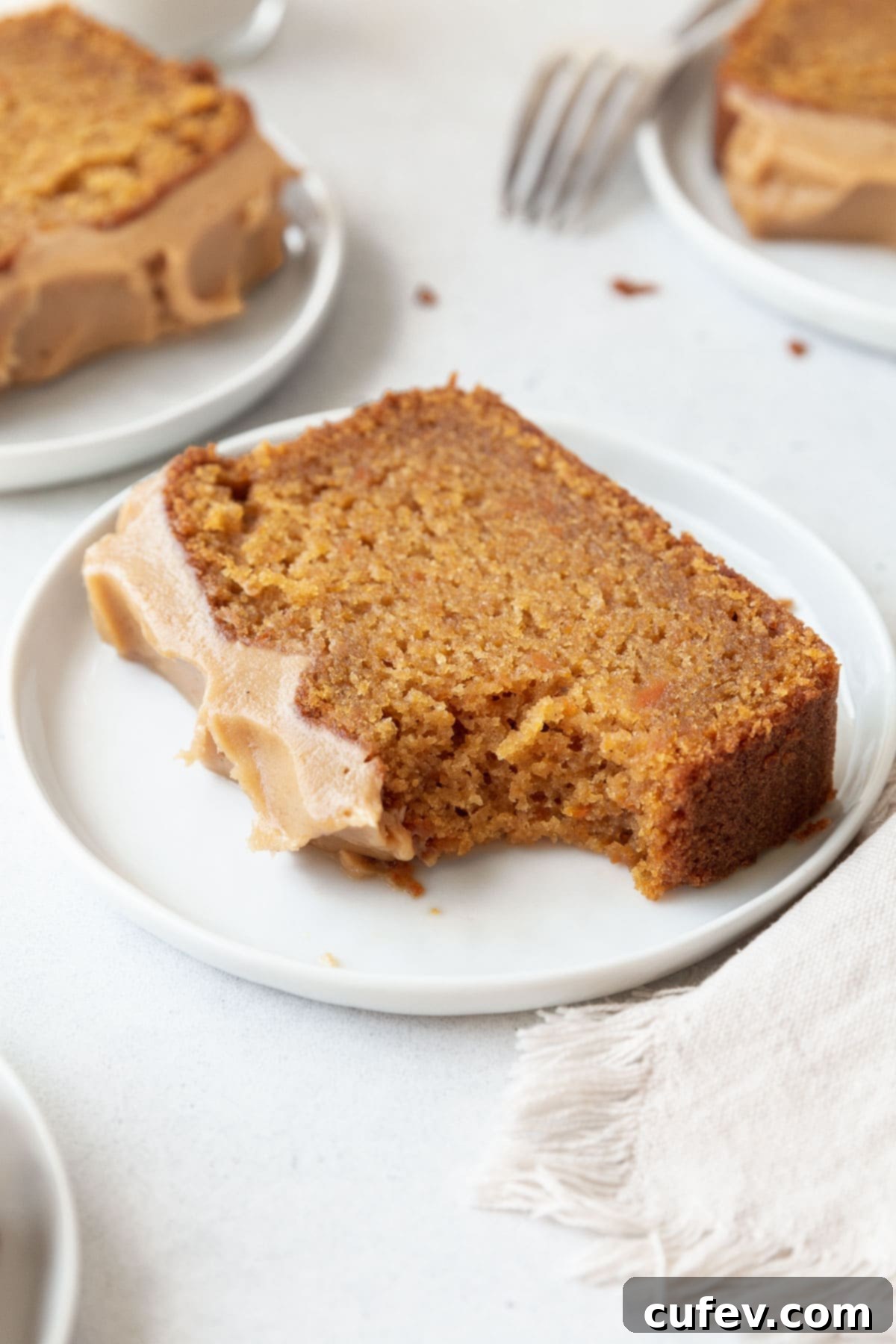 A delicious slice of gluten-free sweet potato cake on a white dessert plate, with a bite taken, revealing its moist interior and creamy frosting.