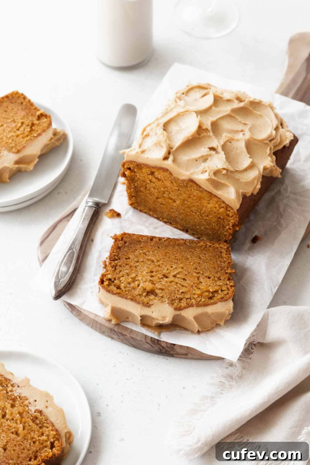 A perfectly sliced loaf of gluten-free sweet potato cake showcasing its moist crumb and topped with luscious maple cashew frosting. A silver knife rests beside it.