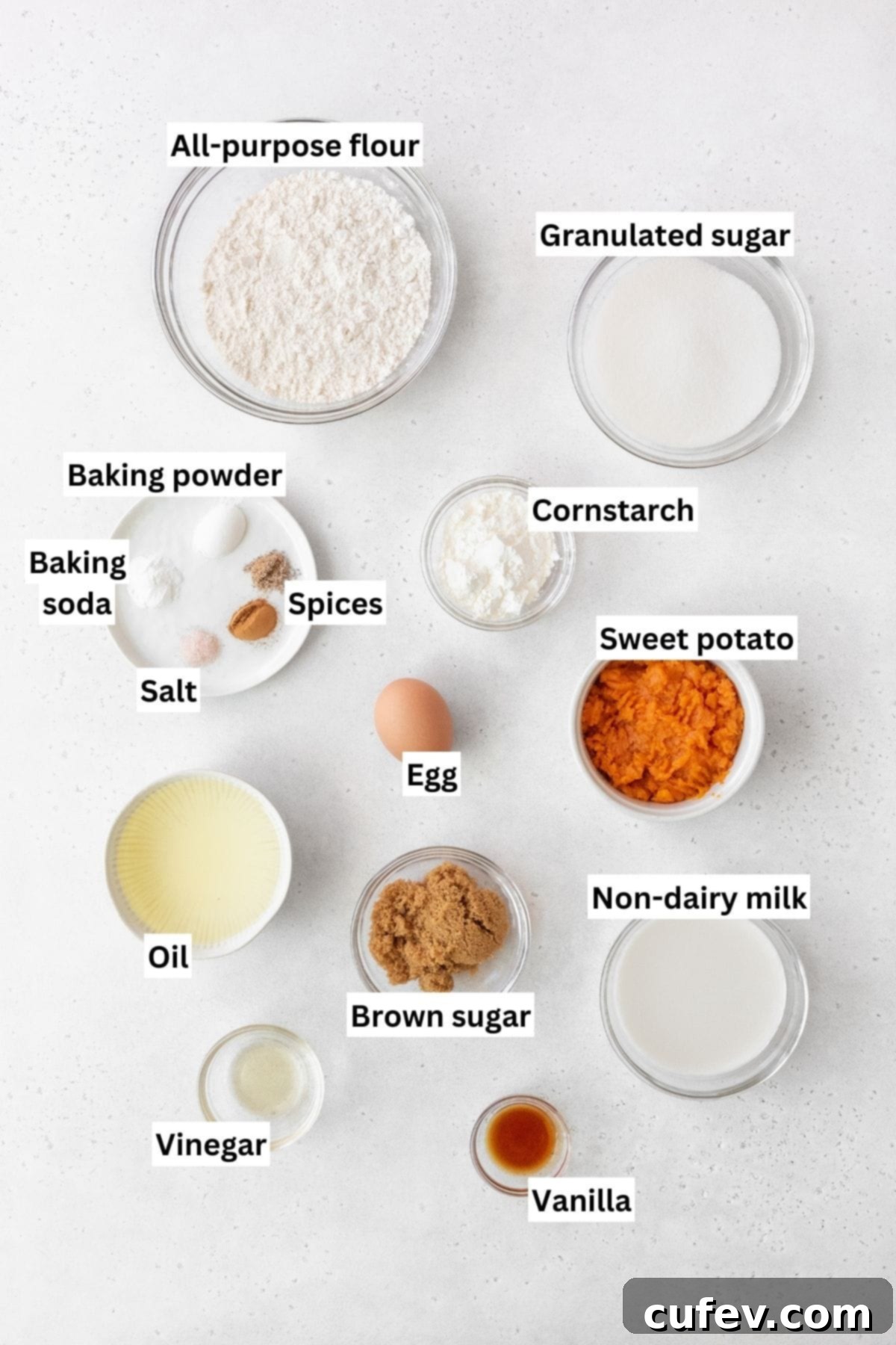 Overhead shot of all the sweet potato cake ingredients meticulously measured out into separate glass bowls on a clean white surface, ready for mixing.