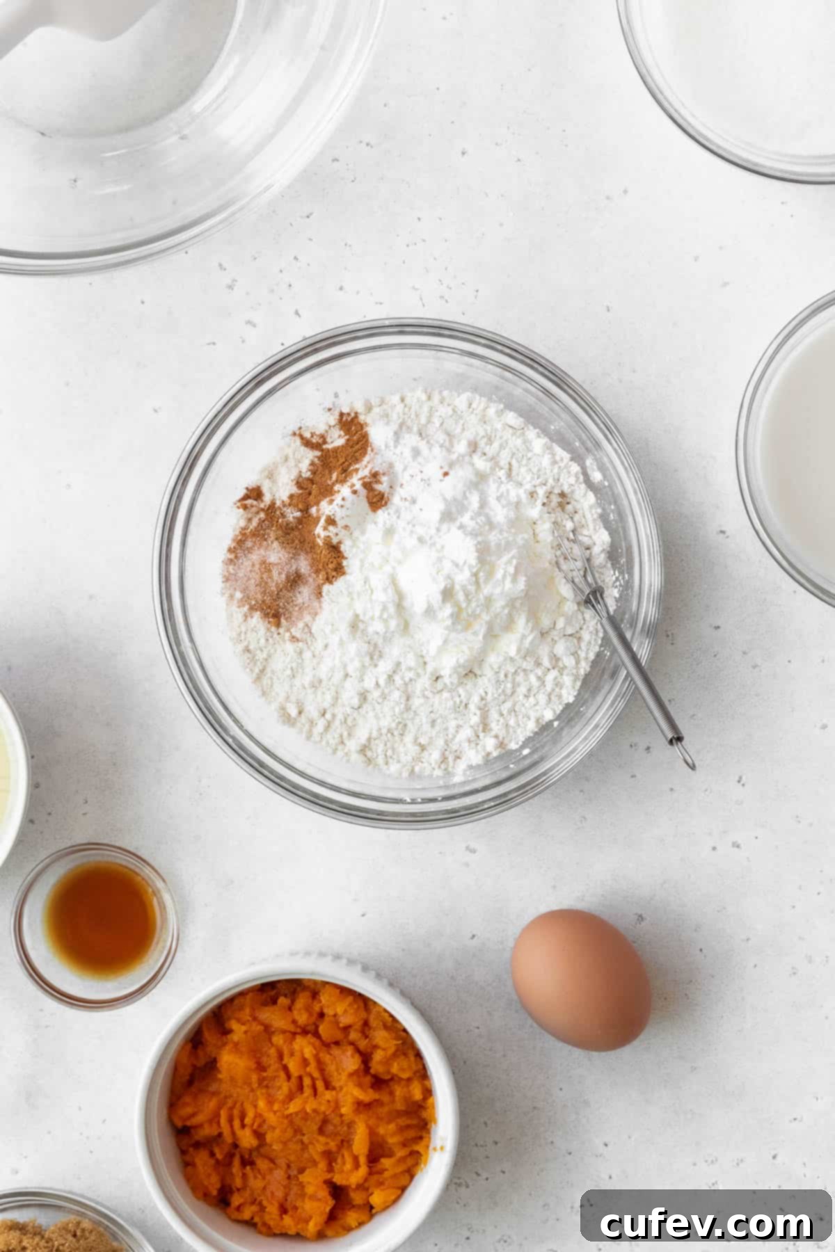 Flour, salt, baking soda, baking powder, and various spices are neatly measured into a glass bowl, ready to be combined for the sweet potato cake batter.