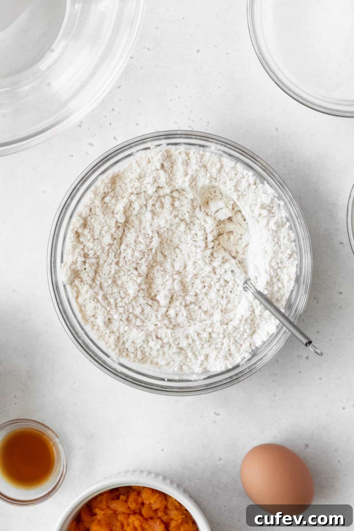 The thoroughly mixed dry ingredients for the sweet potato cake, a uniform blend of flour and spices, settled in a glass bowl.