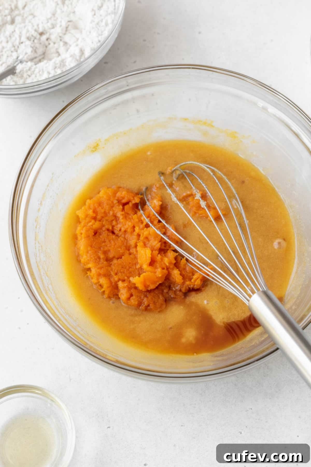Mashed sweet potato and vanilla extract are gently added to the glass bowl of wet ingredients, ready for whisking.