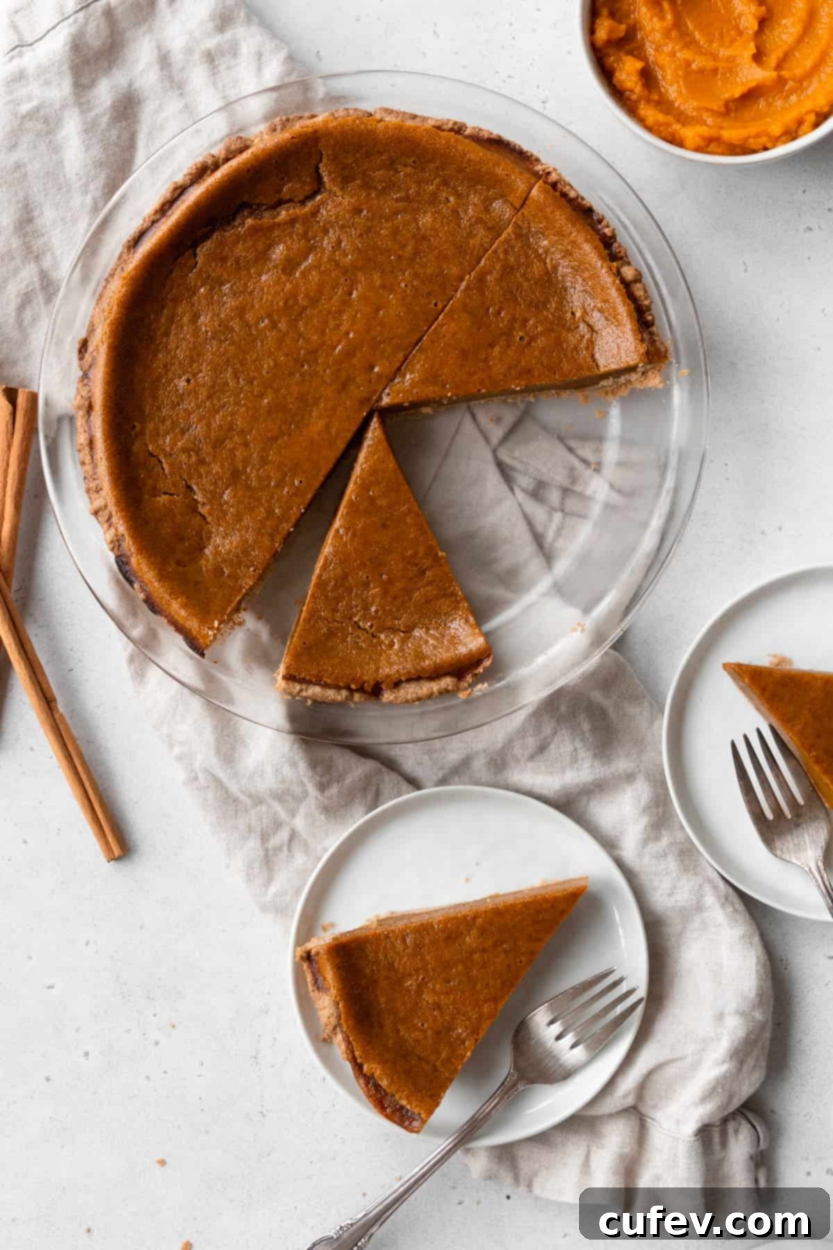 A beautifully sliced egg-free pumpkin pie presented on a natural linen cloth, surrounded by small dessert plates with individual pie slices.