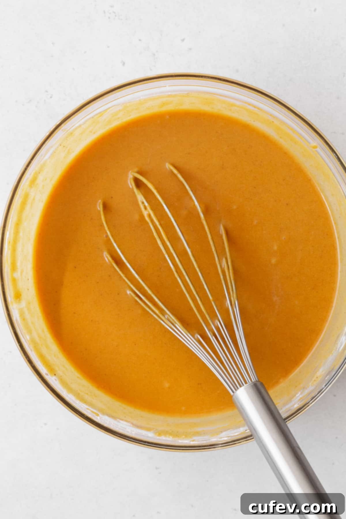 The smooth and creamy vegan pumpkin pie filling in a bowl, perfectly mixed with a whisk.