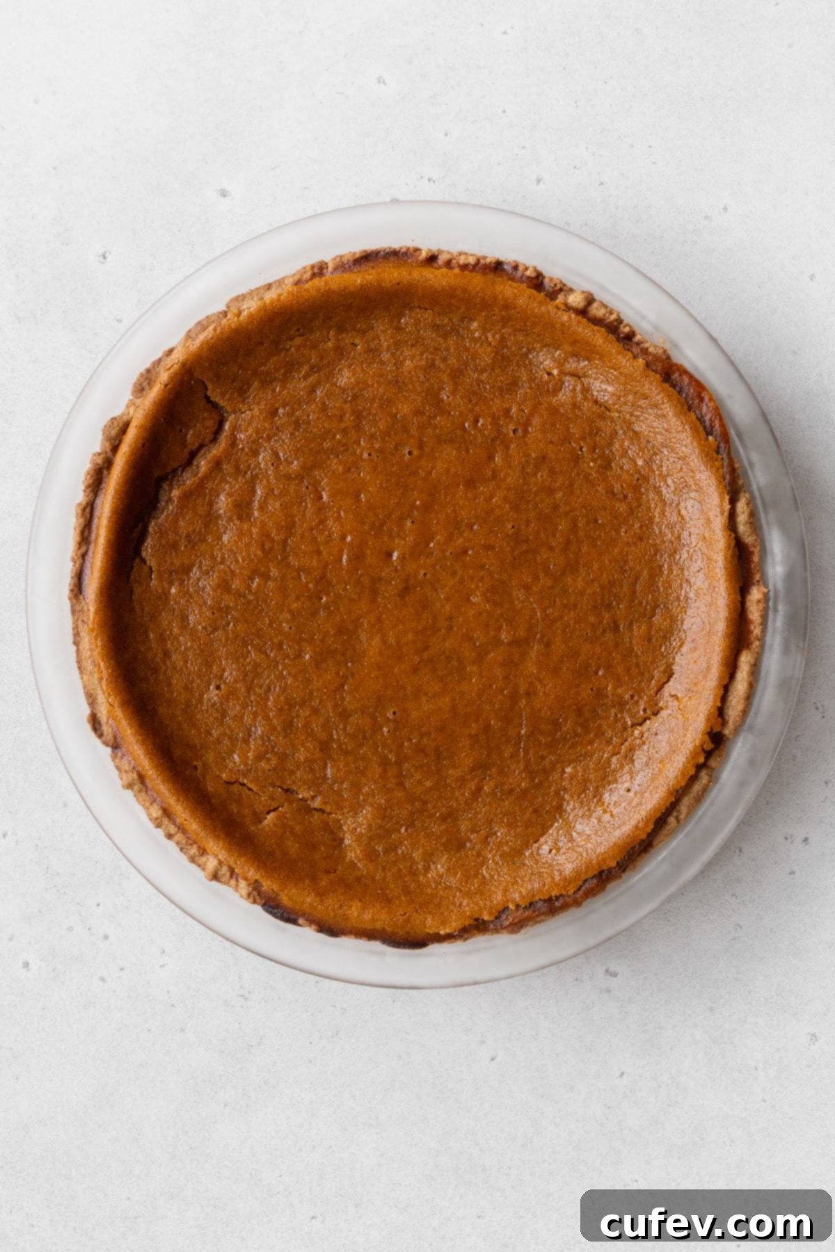 The freshly baked vegan pumpkin pie, golden and inviting, cooling on a white surface.