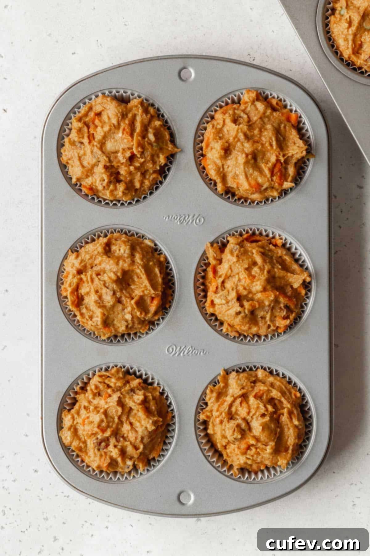 Process shot - 6 cup muffin tin filled with muffin tin liners filled with morning glory muffin batter.