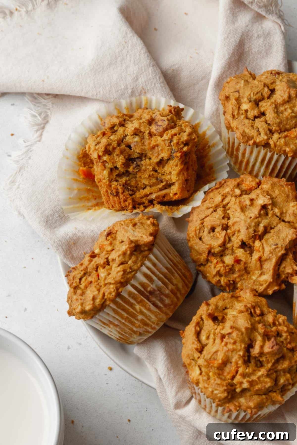 Overhead shot of morning glory muffins with one that has a bite taken out and turned on its side so you can see the moist interior.