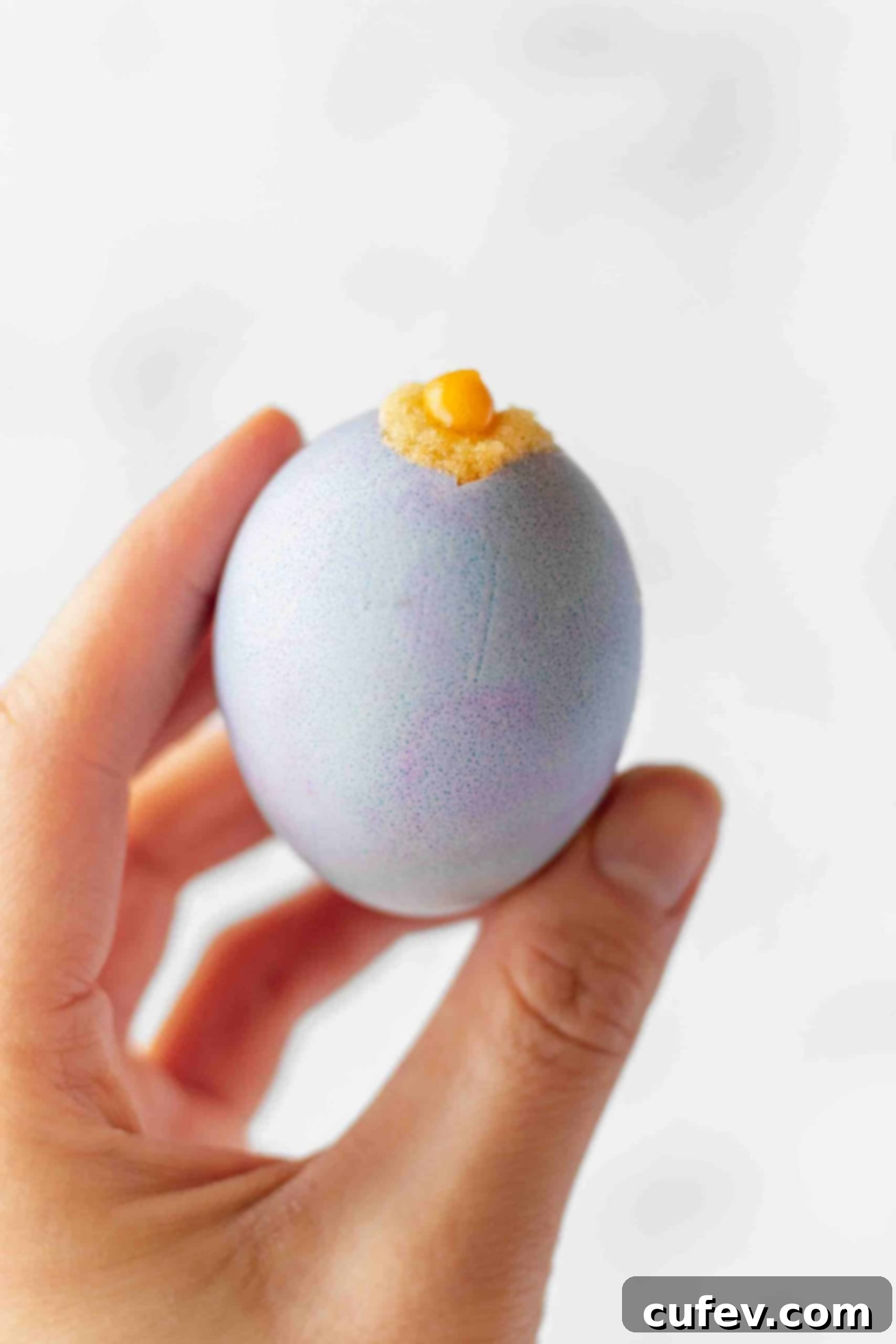 Hand holding a dyed eggshell with a vanilla cake baked inside