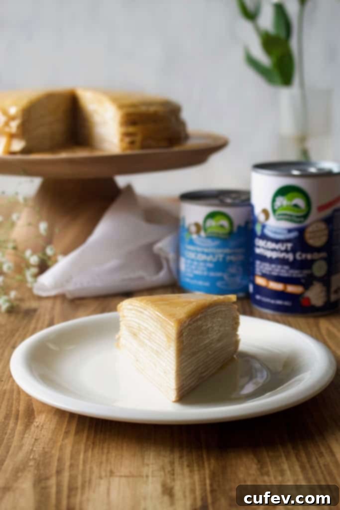 A slice of elegant vegan mille crêpe cake showcasing layers of thin crepes, fluffy coconut whipped cream, and a drizzle of rich homemade dulce de leche on top, ready to be served.