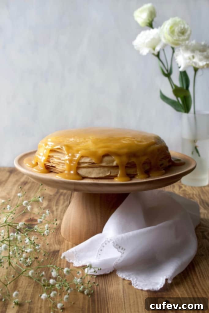 Stack of freshly cooked vegan crepes resting on a wire rack, covered with a tea towel to maintain moisture and warmth, ready for assembly into a cake.