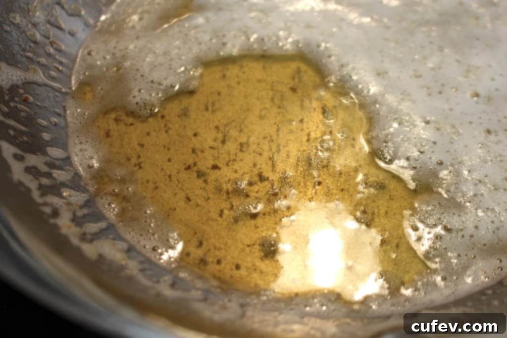 Close-up of butter browning in a saucepan, showing amber-colored milk solids at the bottom through the foam.