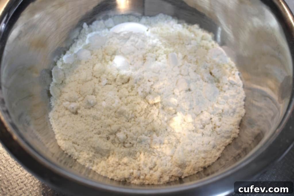 Granulated sugar, almond flour, cake flour, and lemon zest mixed in a bowl, ready for wet ingredients.