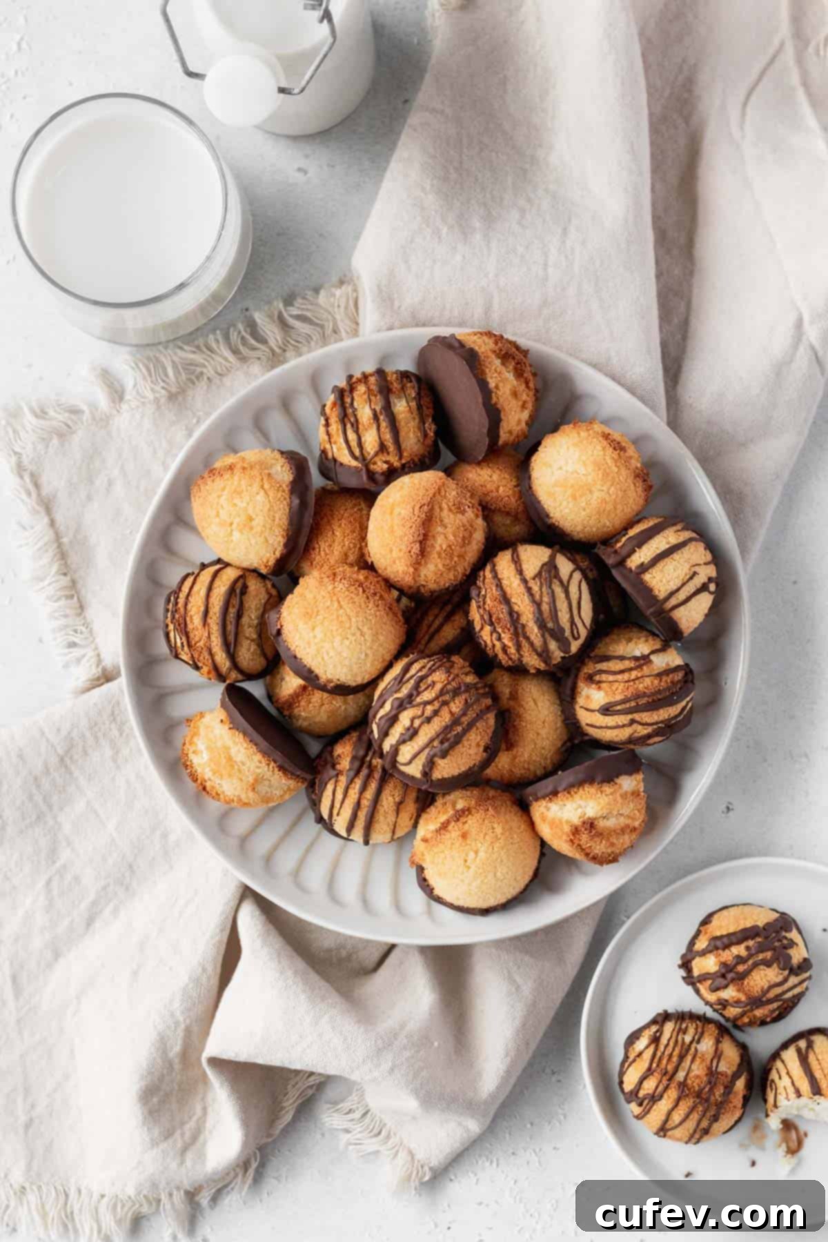Overhead shot featuring both plain and chocolate-drizzled coconut macaroons artfully arranged on a plate, accompanied by a glass of plant-based milk, a smaller plate of cookies, and a natural linen backdrop.