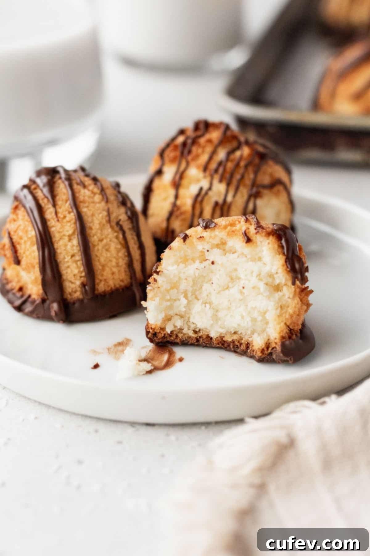Three gluten-free vegan macaroons on a white plate, one with a bite taken out of it, showing its chewy interior.