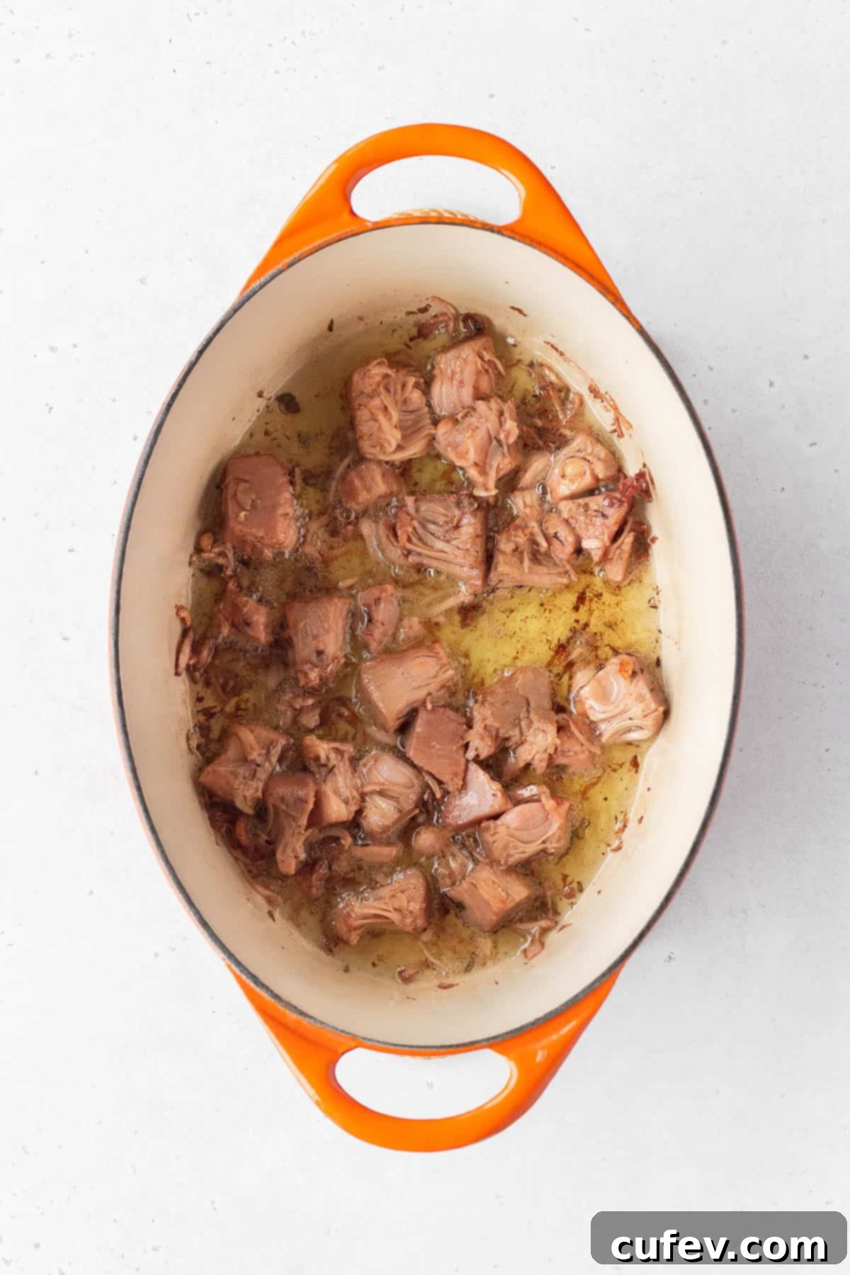 Young green jackfruit confit being cooked in oil in a pot.