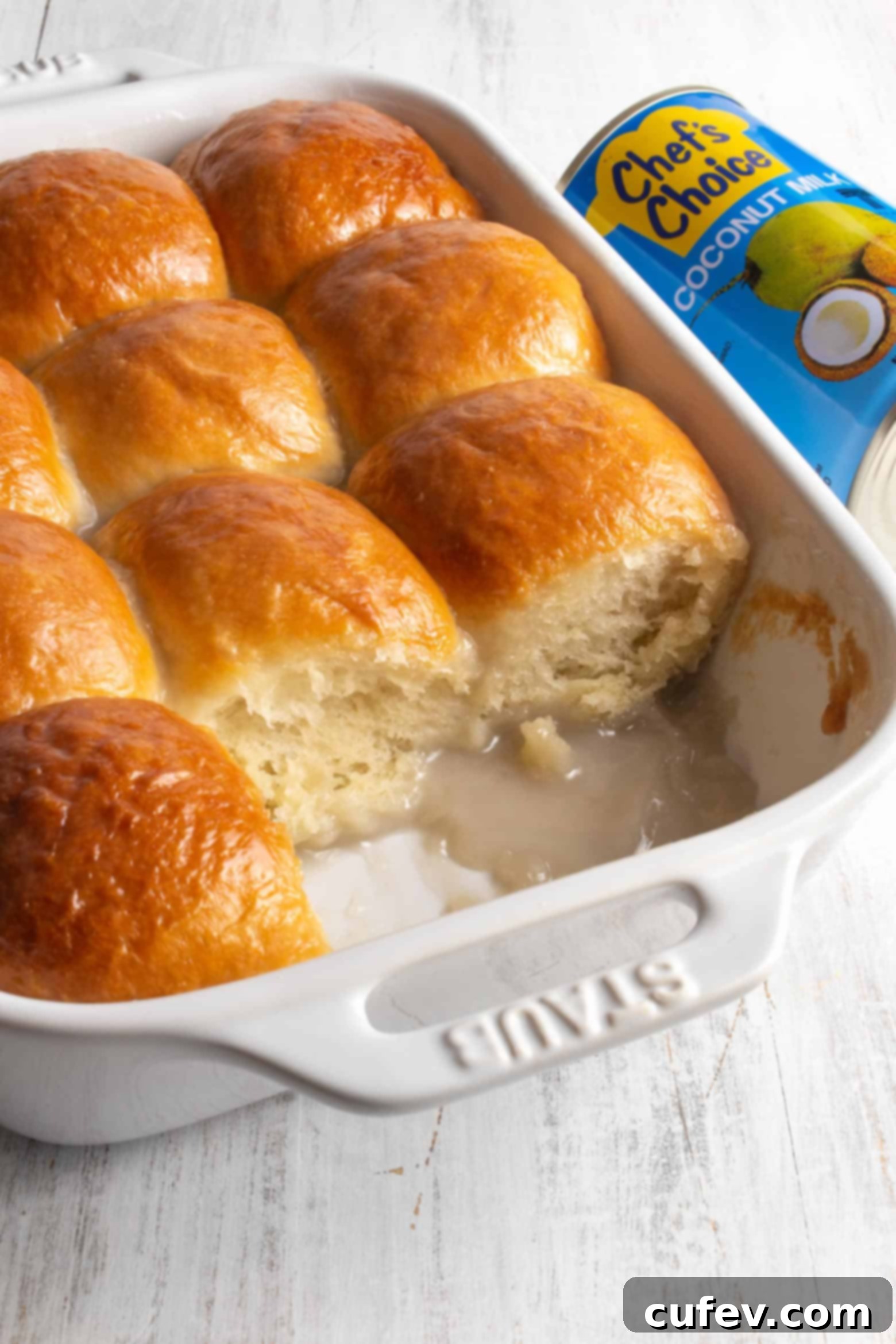 Freshly baked sweet coconut buns in a white rectangular baking dish, golden brown and glistening with coconut sauce.