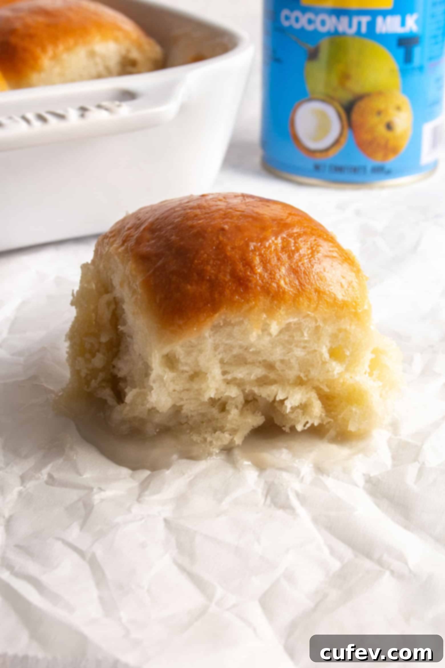 A single pani popo, a sweet Samoan coconut roll, resting on parchment paper, glistening with glaze.