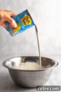 Pouring a can of coconut milk into a large bowl with flour and other ingredients.