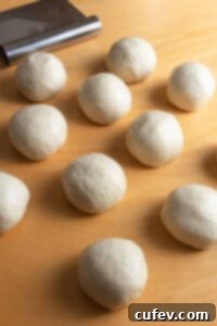 Twelve neatly arranged balls of bread dough in a baking dish, ready for their second rise.