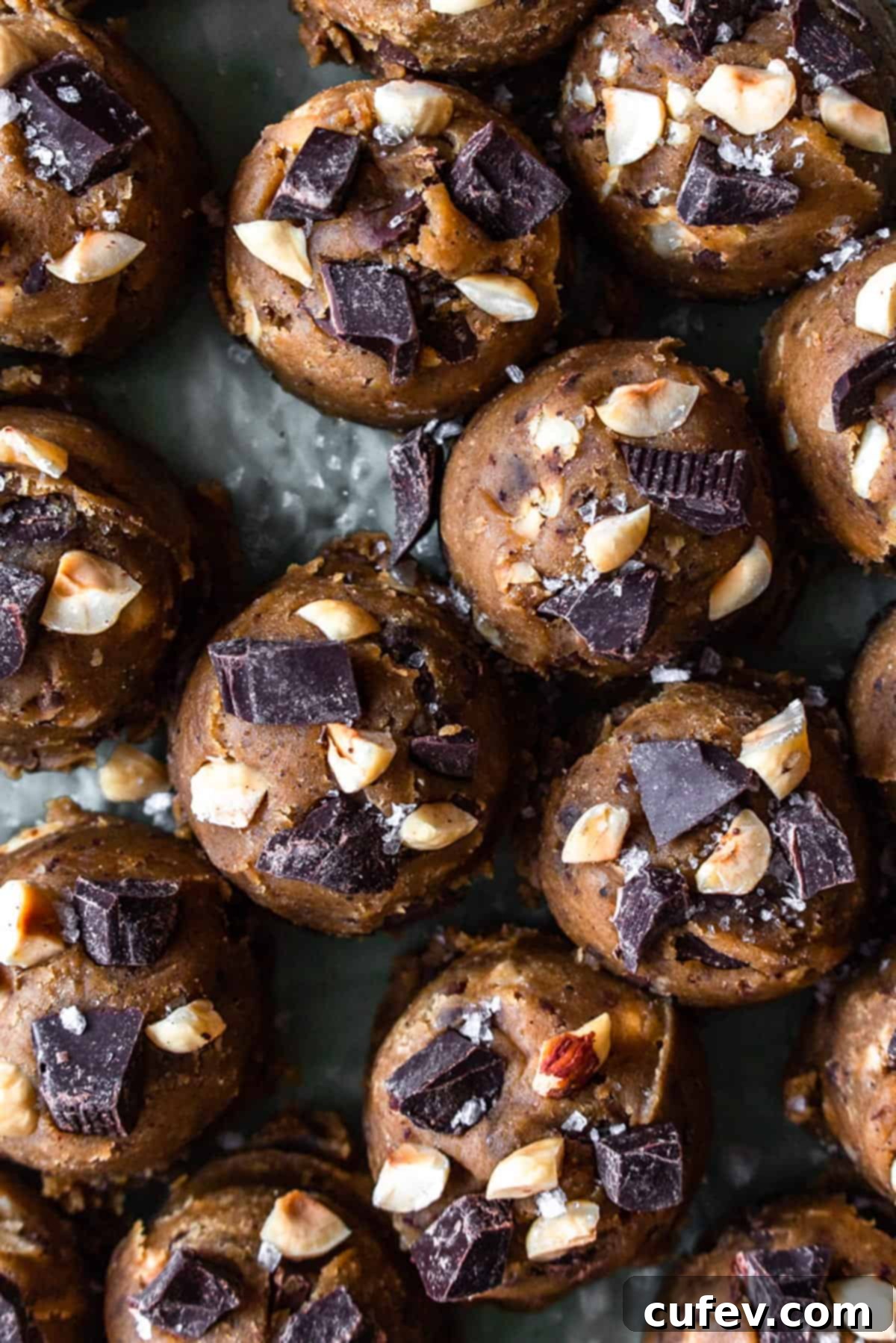 Raw brown butter cookie dough balls, generously topped with chopped chocolate and toasted hazelnuts, ready for baking.