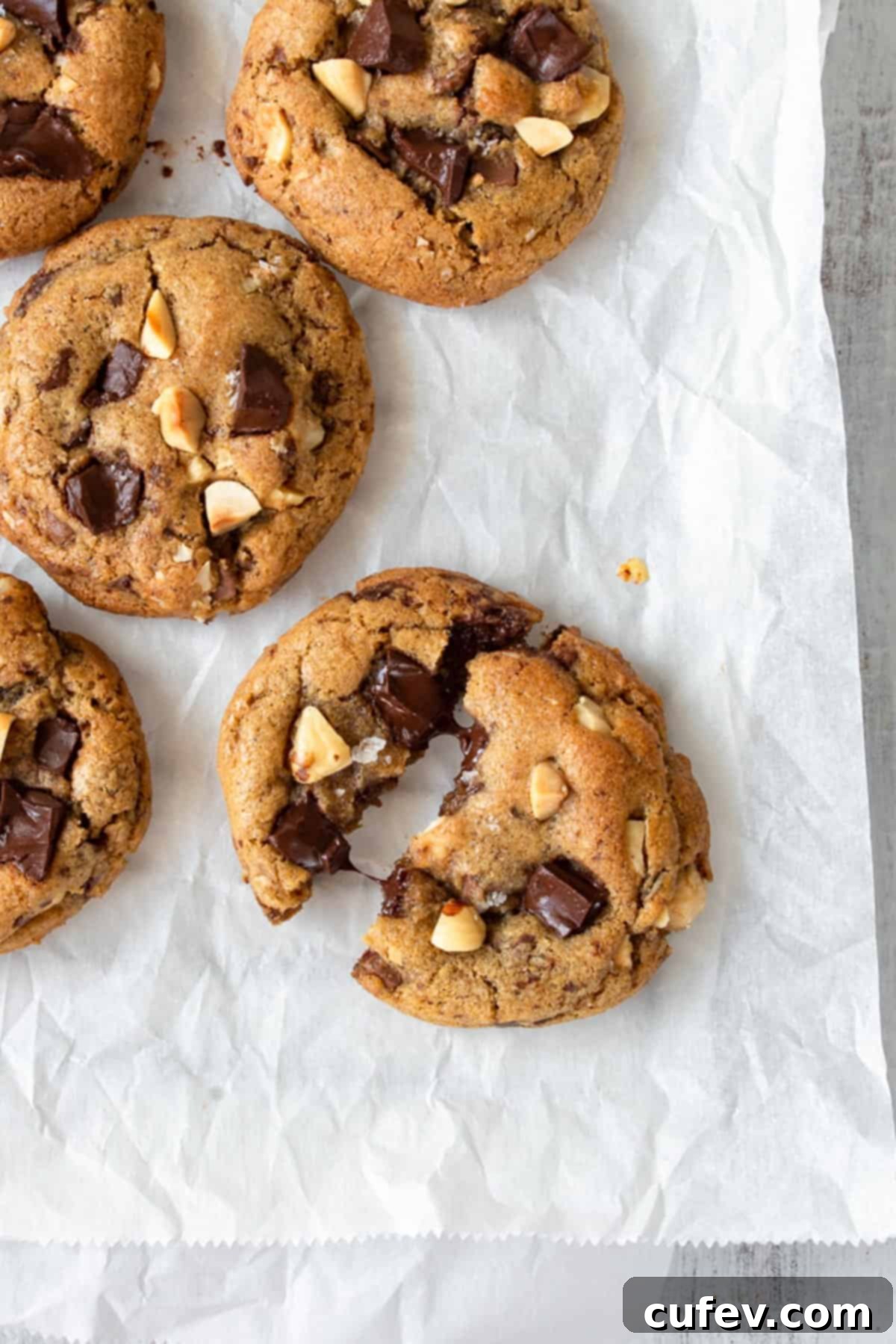 A perfectly baked brown butter chocolate chip cookie broken in half, revealing its soft, gooey center with melted chocolate, with more cookies in the background.