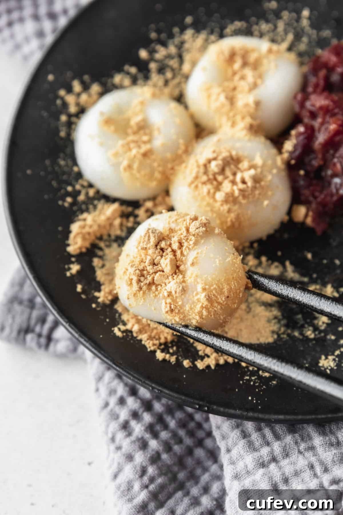 Black chopsticks picking up a shiratama dango with kinako powder on top.