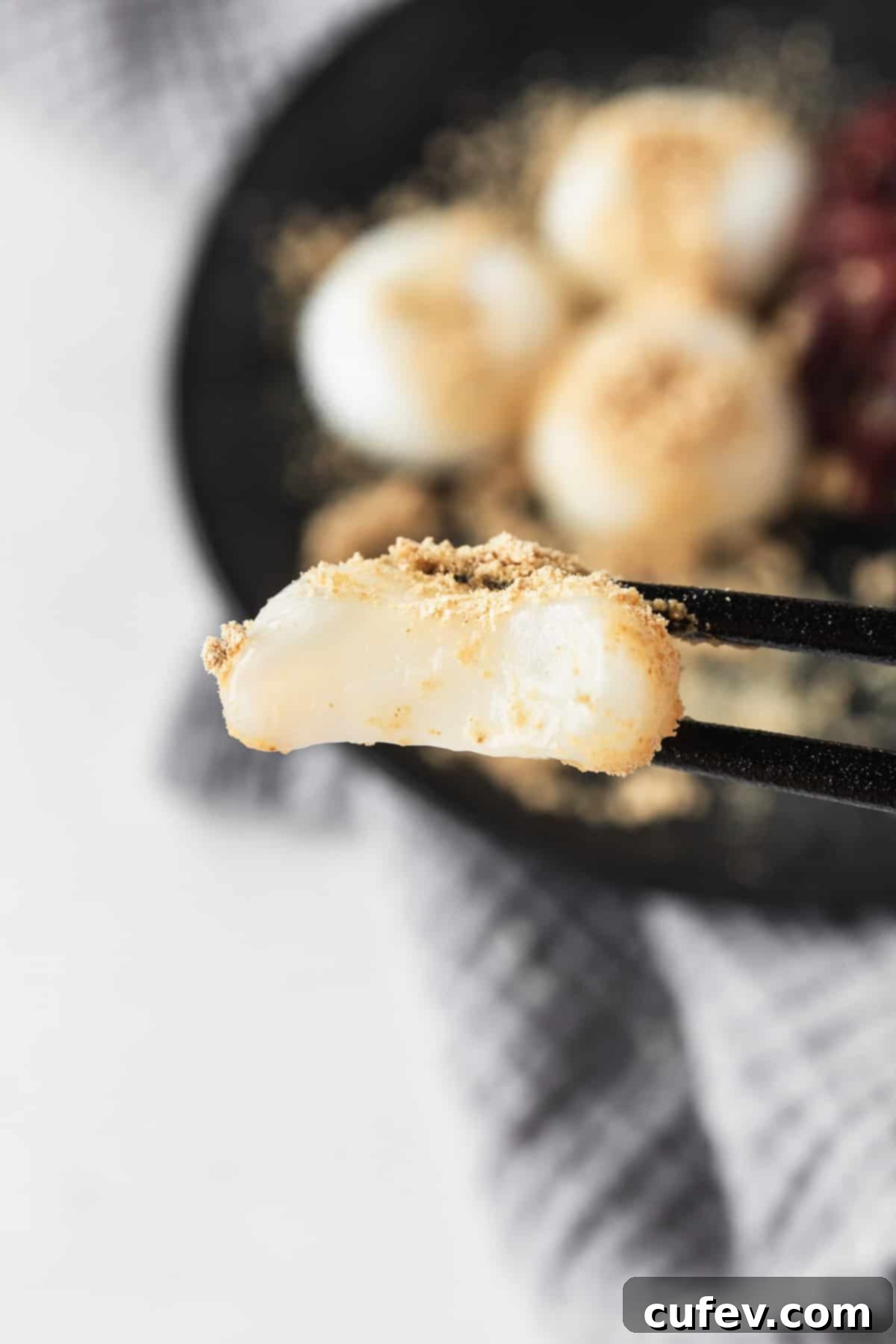 A bitten shiratama mochi being held by black chopsticks.