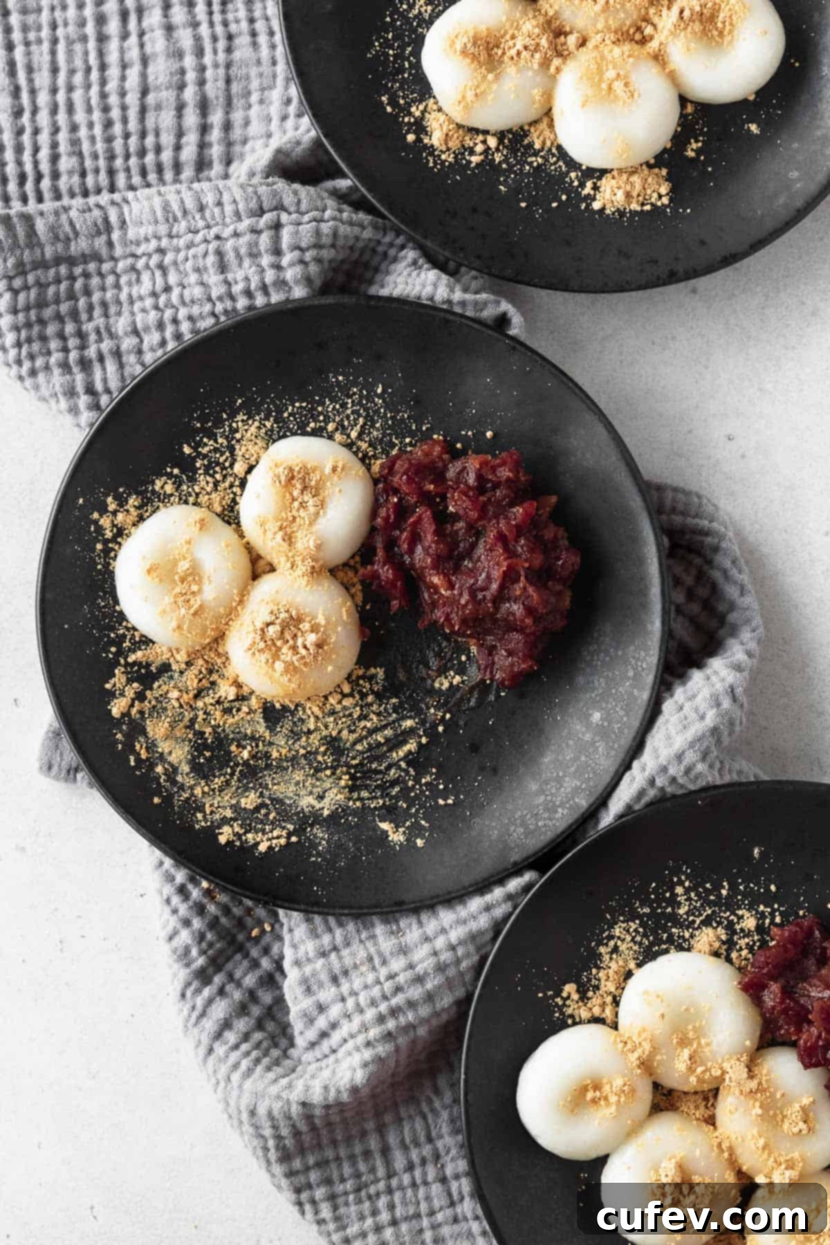 A half eaten black plate of shiratama and anko on a grey linen napkin.