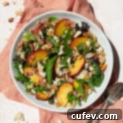 Peach salad in a white bowl on a peach colored linen, with a spoon and fork on the side.