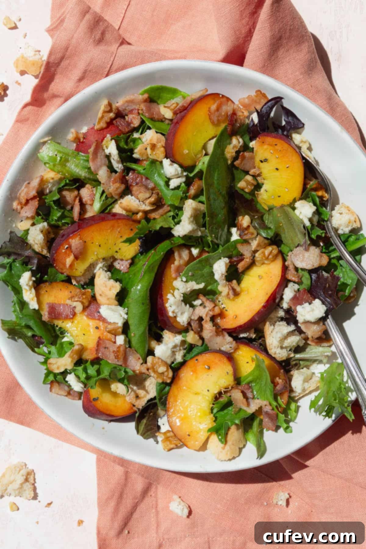 Peach salad in a white bowl on a peach colored background.
