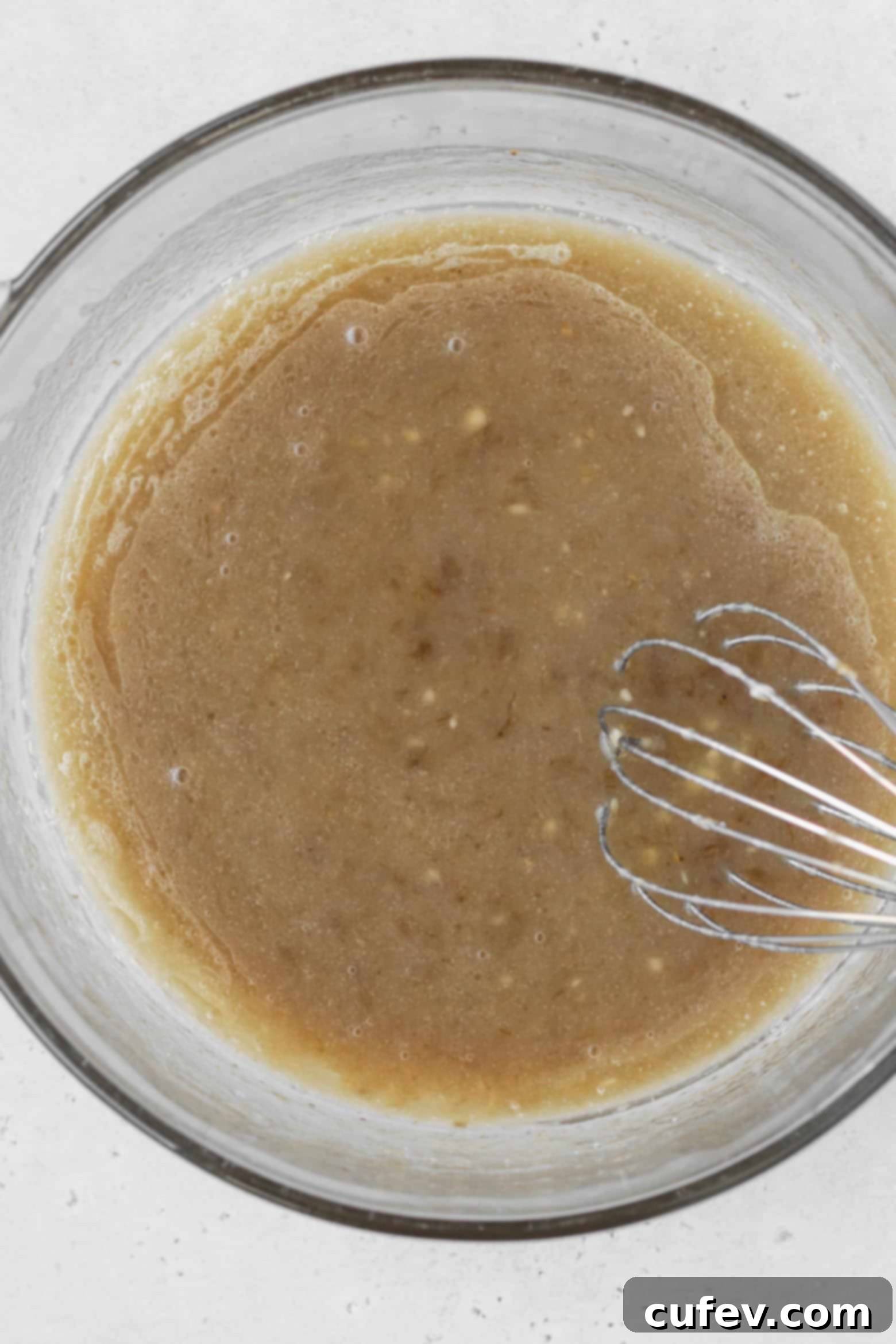 A bowl containing oil, mashed banana, sugar, milk, apple cider vinegar, and vanilla extract, thoroughly mixed together.