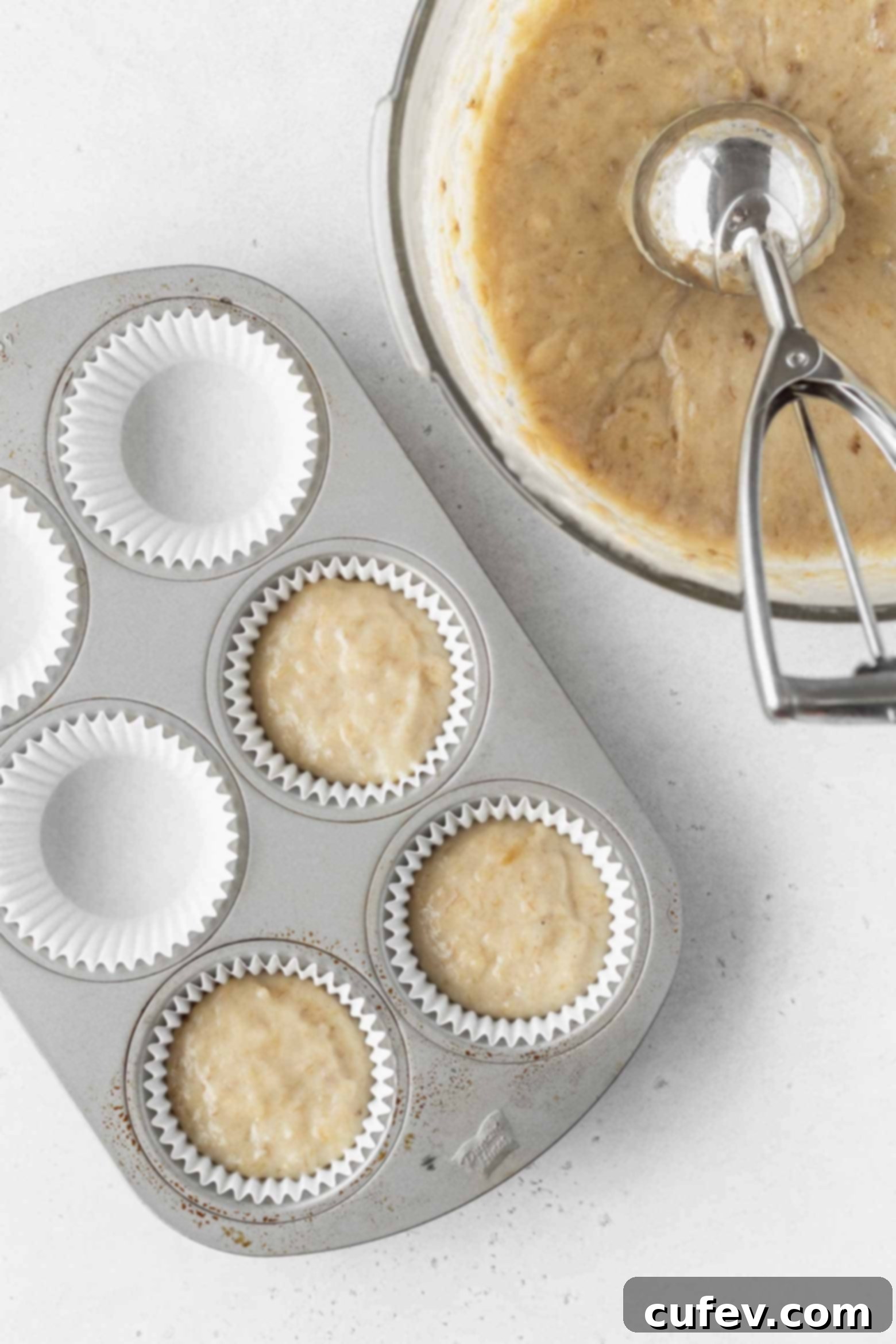 Vegan banana cupcake batter being scooped into a cupcake pan using an ice cream scoop, demonstrating the easy process.