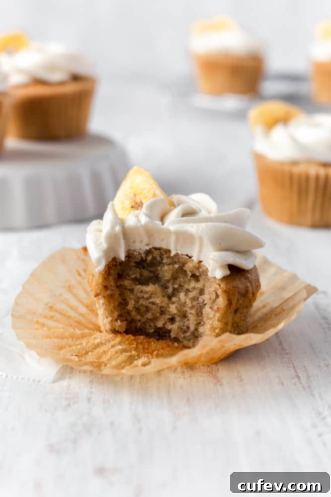 A bitten banana cupcake showing the moist, fluffy inside, topped with buttercream frosting.