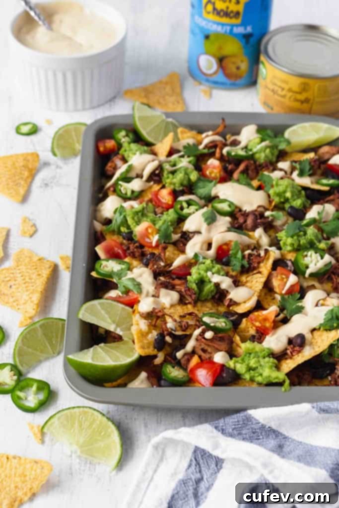A vibrant platter of vegan nachos loaded with jackfruit, black beans, tomatoes, guacamole, jalapeños, cilantro, and creamy cashew queso. Perfect for a plant-based party appetizer.
