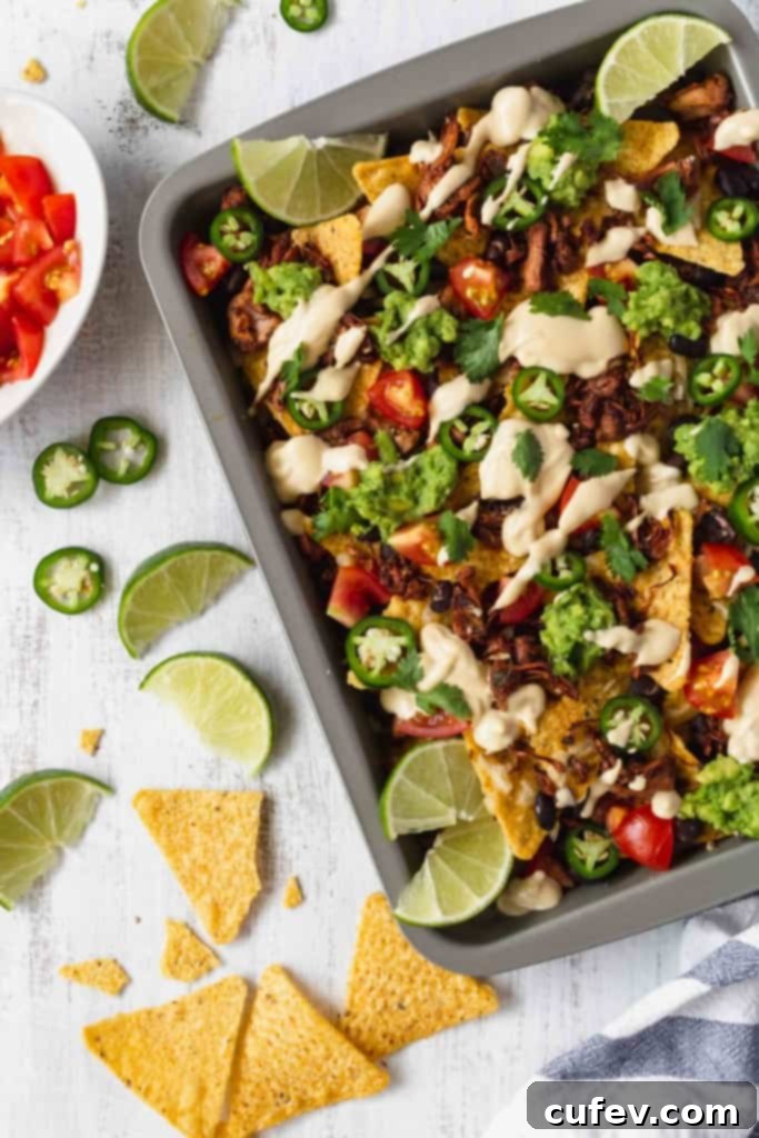 A close-up of a generous serving of vegan jackfruit nachos with a spoon scooping up creamy vegan queso, black beans, and fresh toppings.