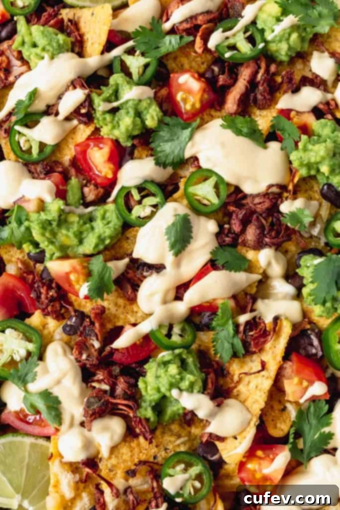 A large platter of perfectly assembled vegan nachos before the final toppings, showing layers of tortilla chips, jackfruit, and black beans.