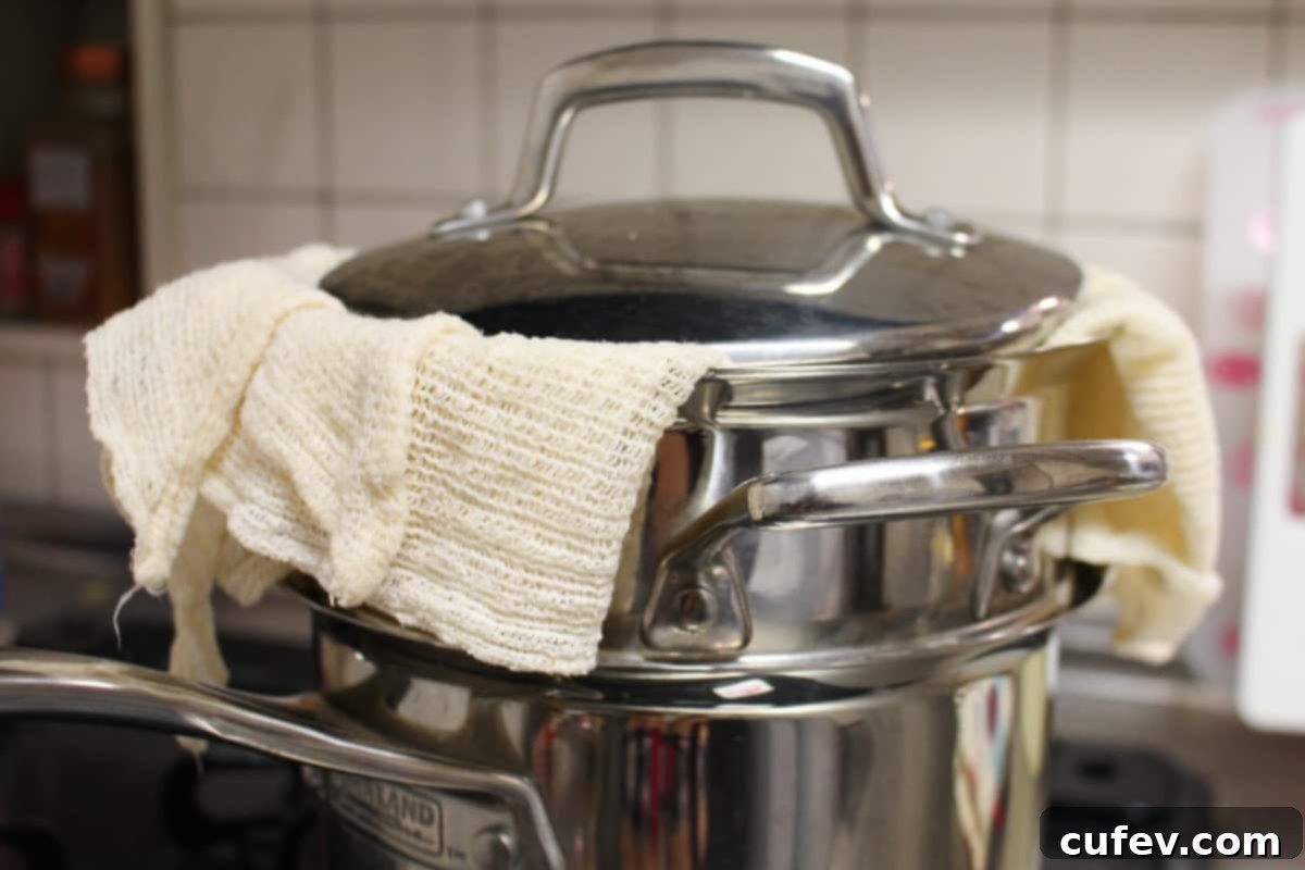 A steamer setup showing a piece of cheesecloth strategically placed under the lid to collect condensation and prevent drips onto the mochi below, ensuring a perfectly dry surface.