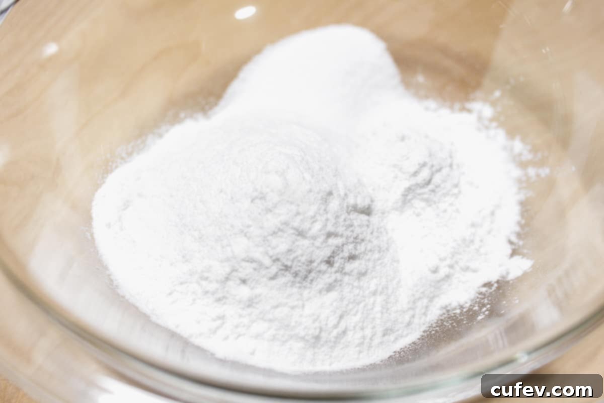 All the dry ingredients for mochi—joshinko rice flour, mochi flour, and granulated sugar—carefully measured and added to a mixing bowl, awaiting the addition of liquid.