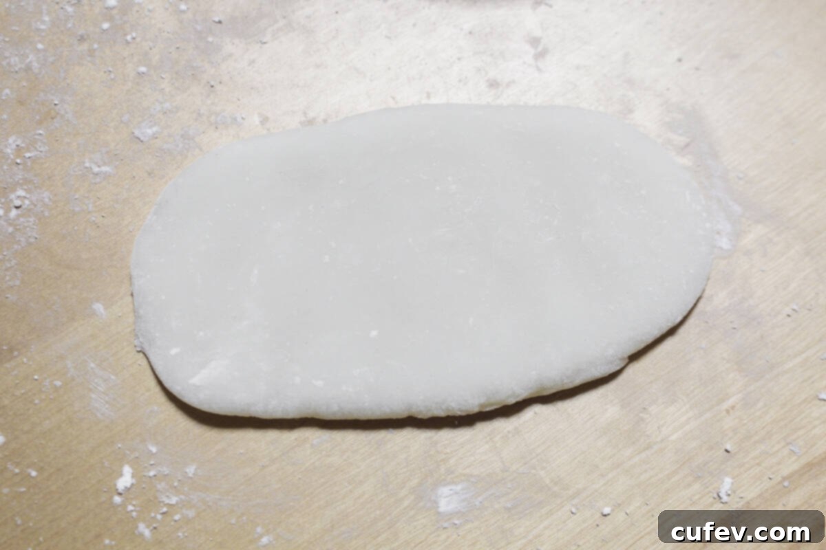 The soft mochi dough being carefully rolled out into an oblong shape, creating the perfect base for the sweet red bean paste filling.