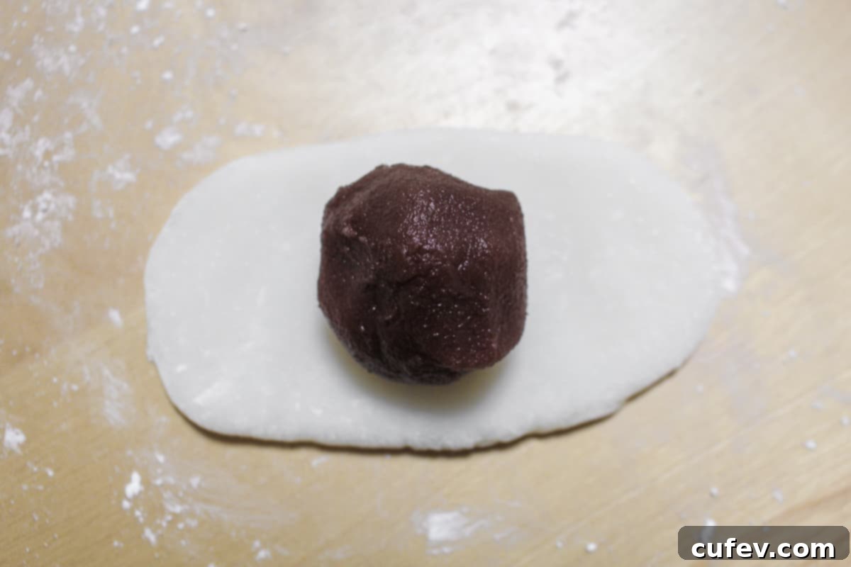 A perfectly portioned ball of sweet red bean paste (anko) neatly placed in the center of the rolled-out mochi dough, ready to be wrapped.